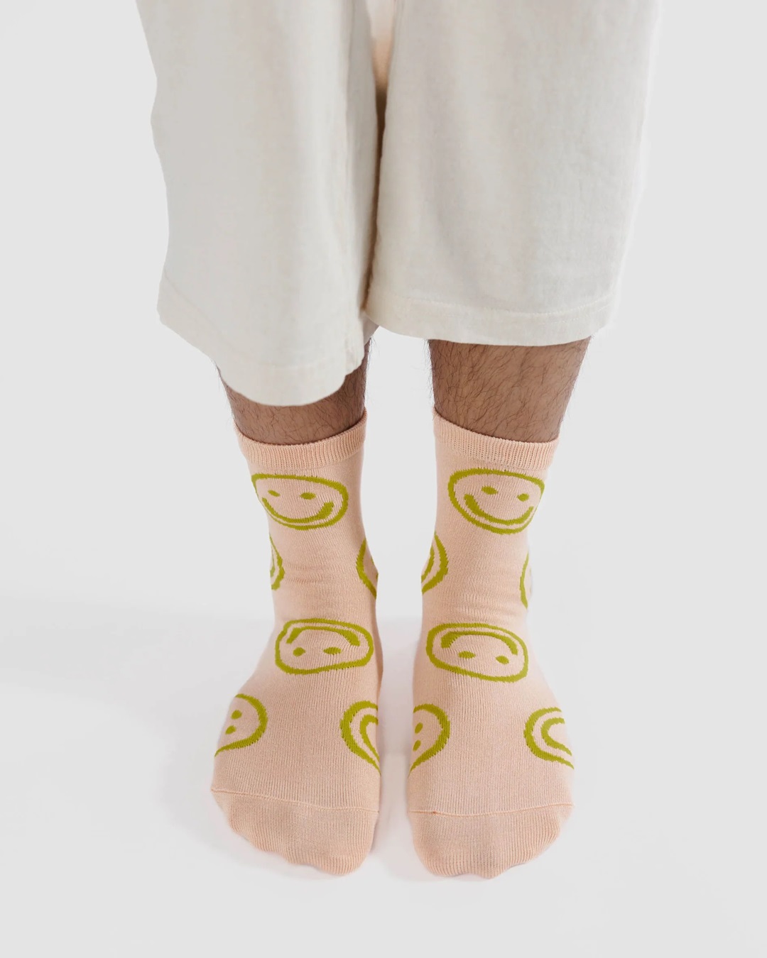 Light pink with green smiley faces pair of socks on feet