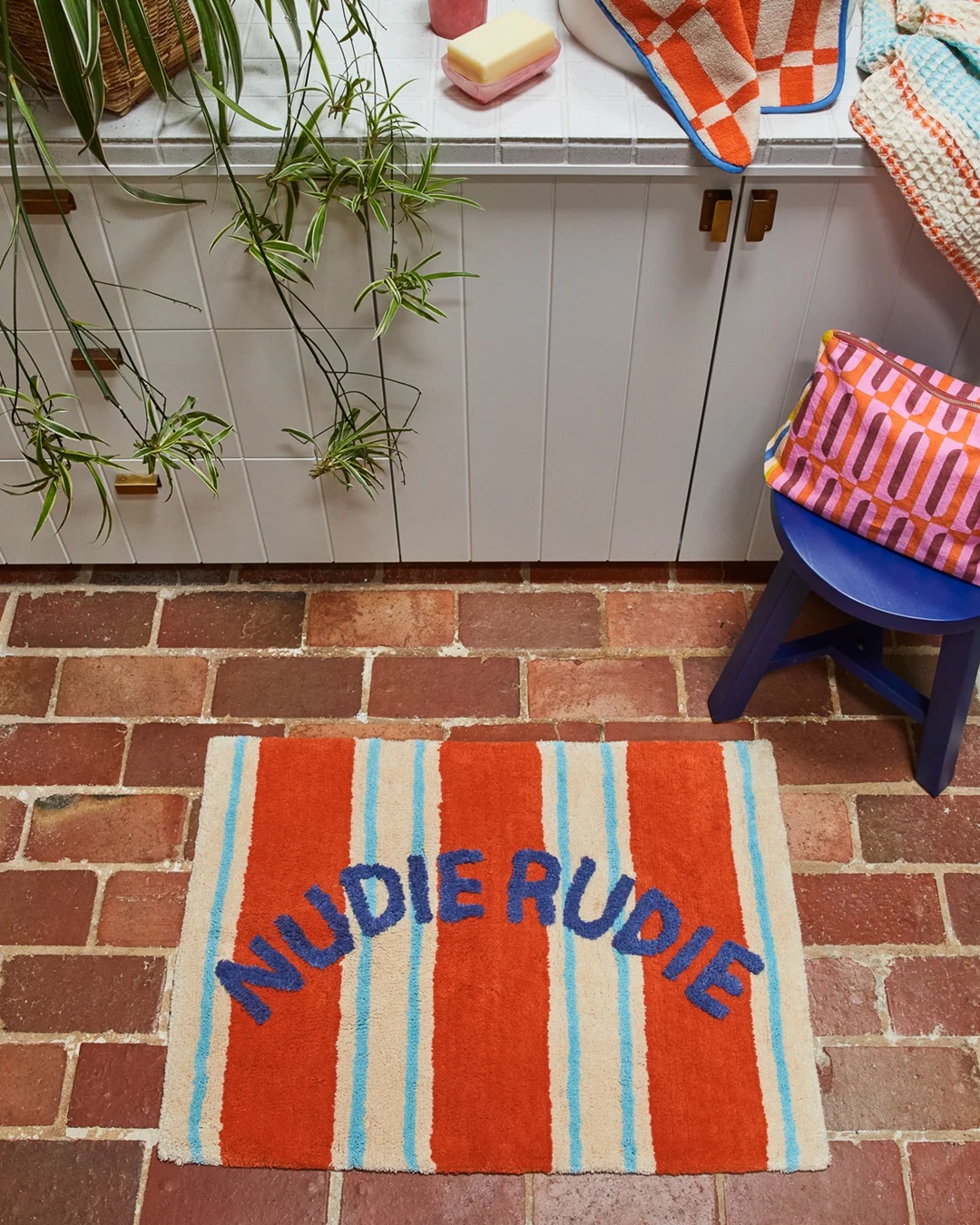 Orange and blue stripe Nudie Rudie bath mat on brick floor bathroom