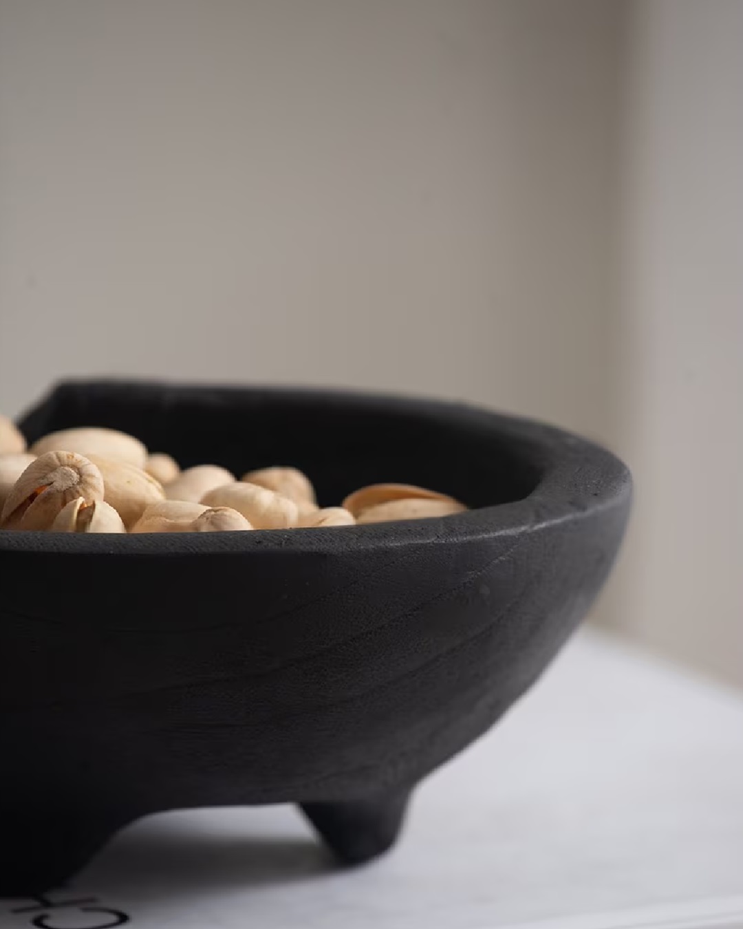 Black teak bowl with feet and nuts inside