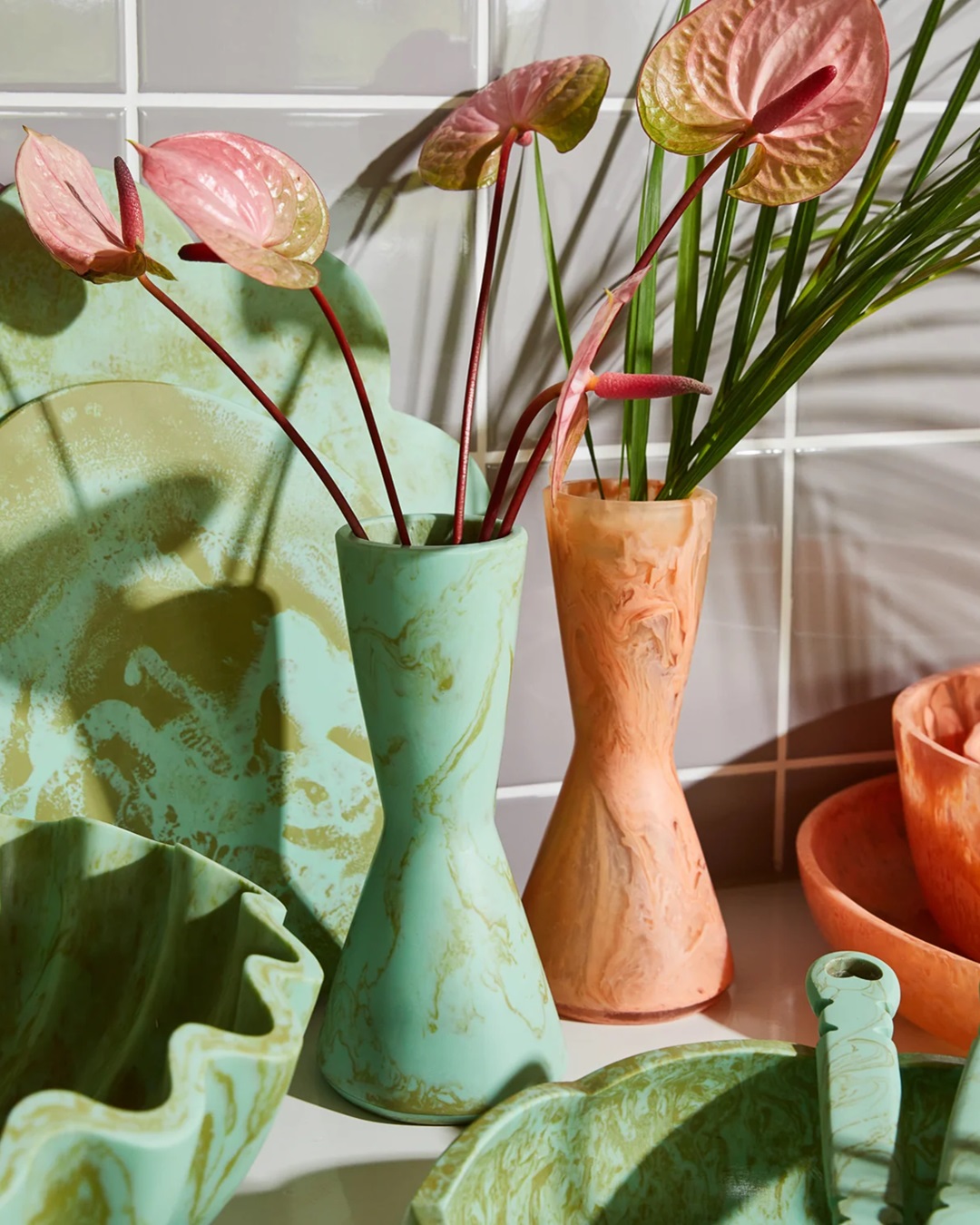 Green and orange resin vases with flowers in on bench