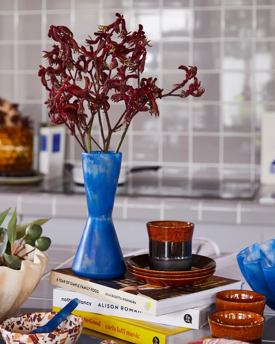 Blue coloured resin vase on bench with other household items