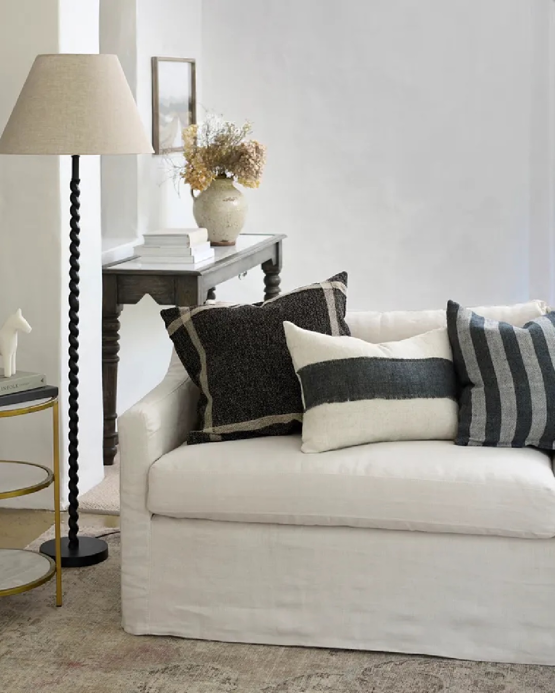 Black and white cushions on white couch with lamp and console next to them