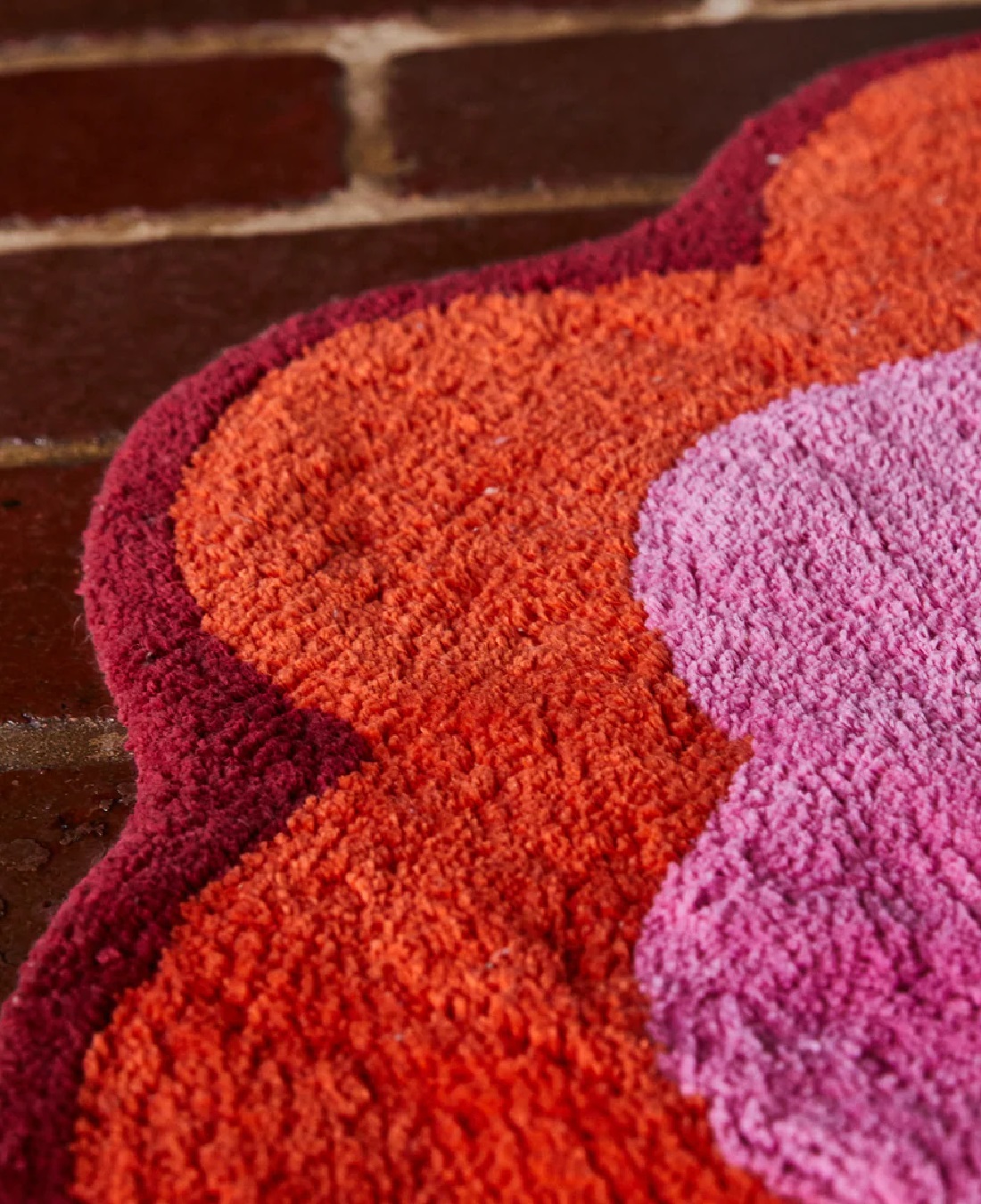 Orange, pink and yellow flower bath mat on brick floor