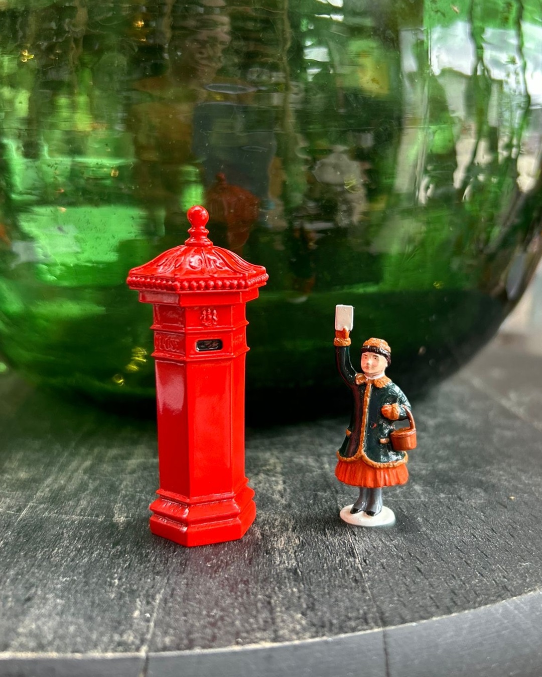 Red letter box and girl posting letter ornament on bench with green glass vase behind