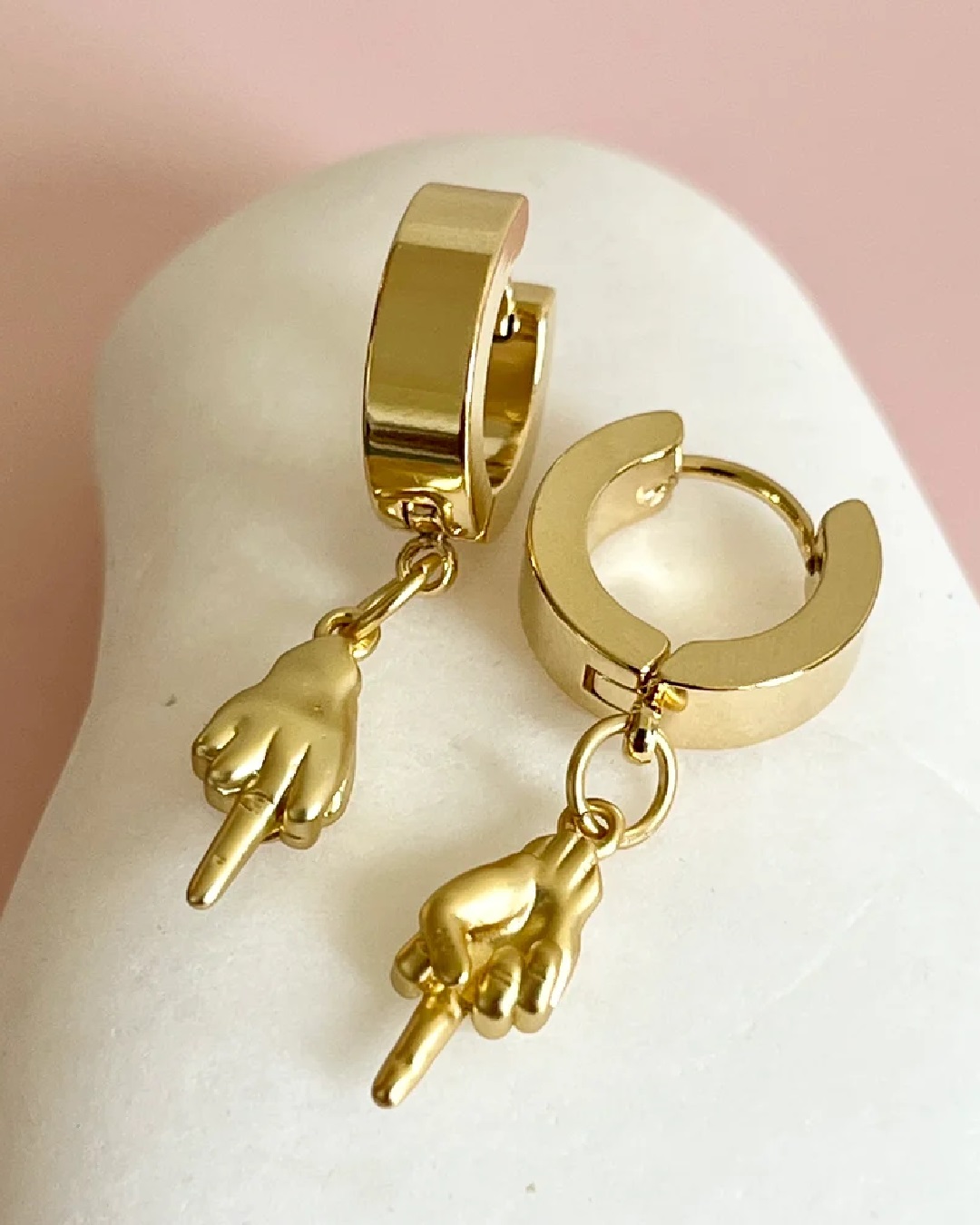 Gold middle finger charm hanging off gold hoop earrings