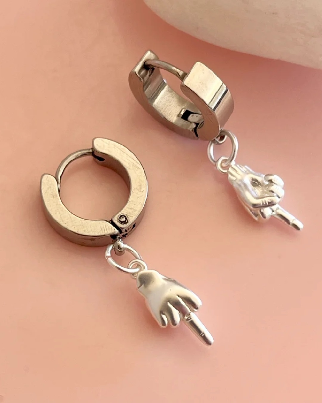 Silver middle finger charm hanging off gold hoop earrings
