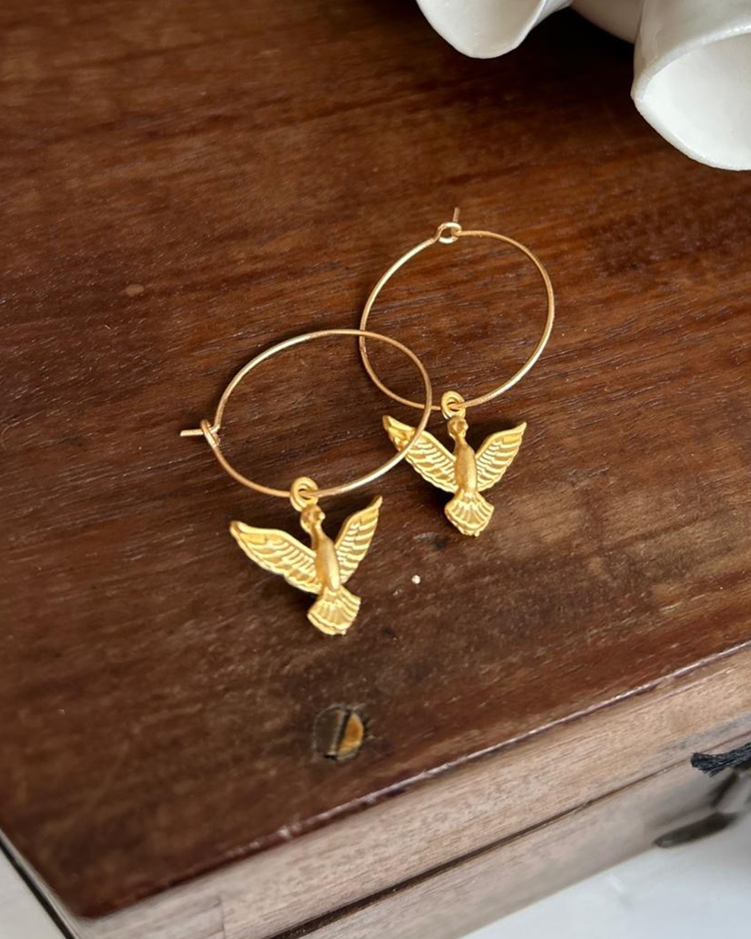 Gold hoop eearrings with gold bird charm on wooden bench