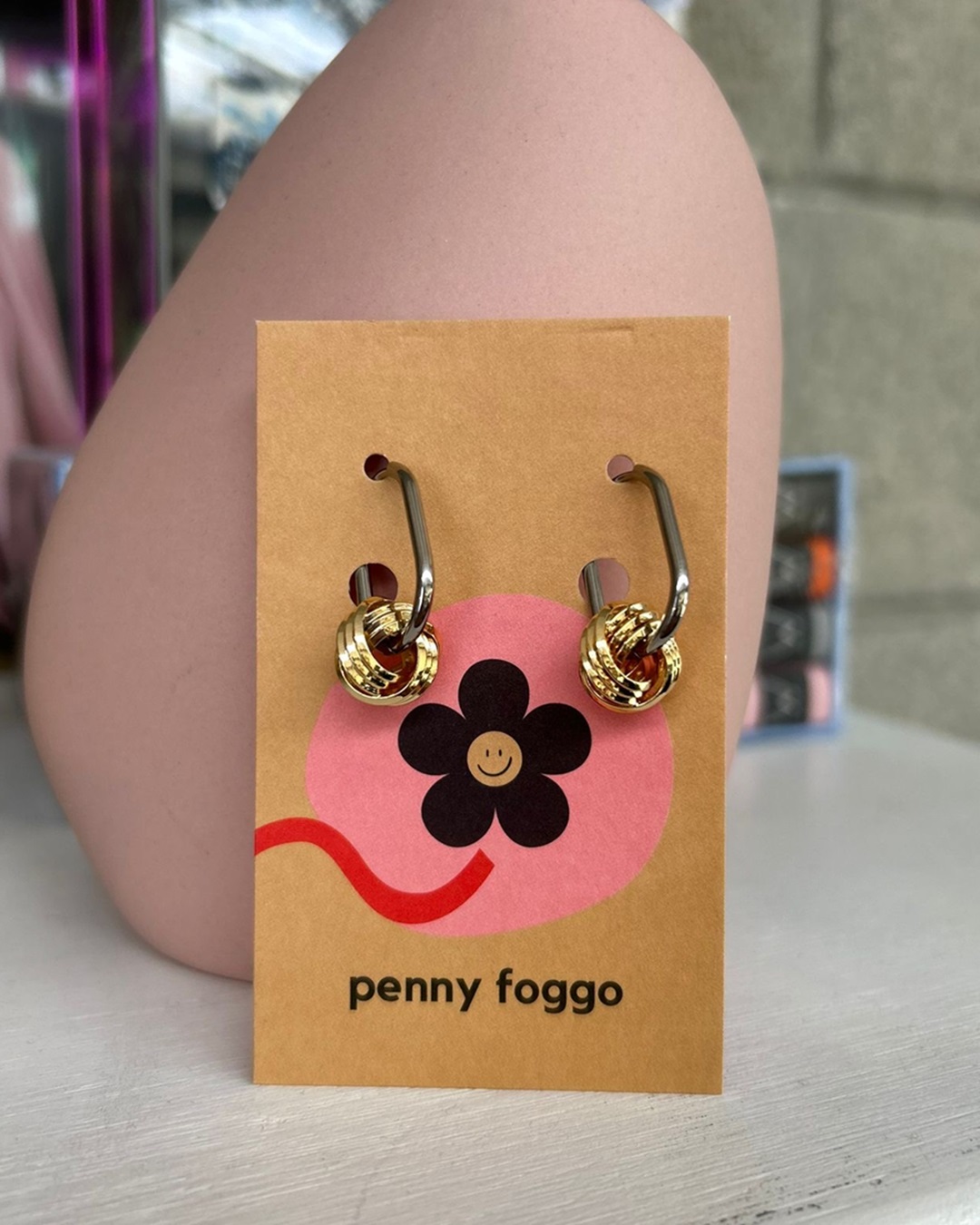Hoop earrings with gold knots in front of pink vase