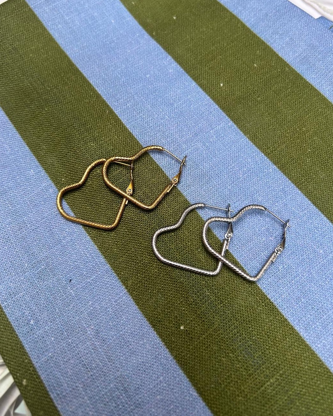 Gold and silver heart earrings on blue and green stripe cloth