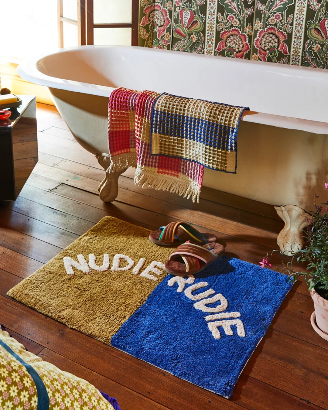 Blue and green Nudie rudie bath mat in front of bath on wooden floor
