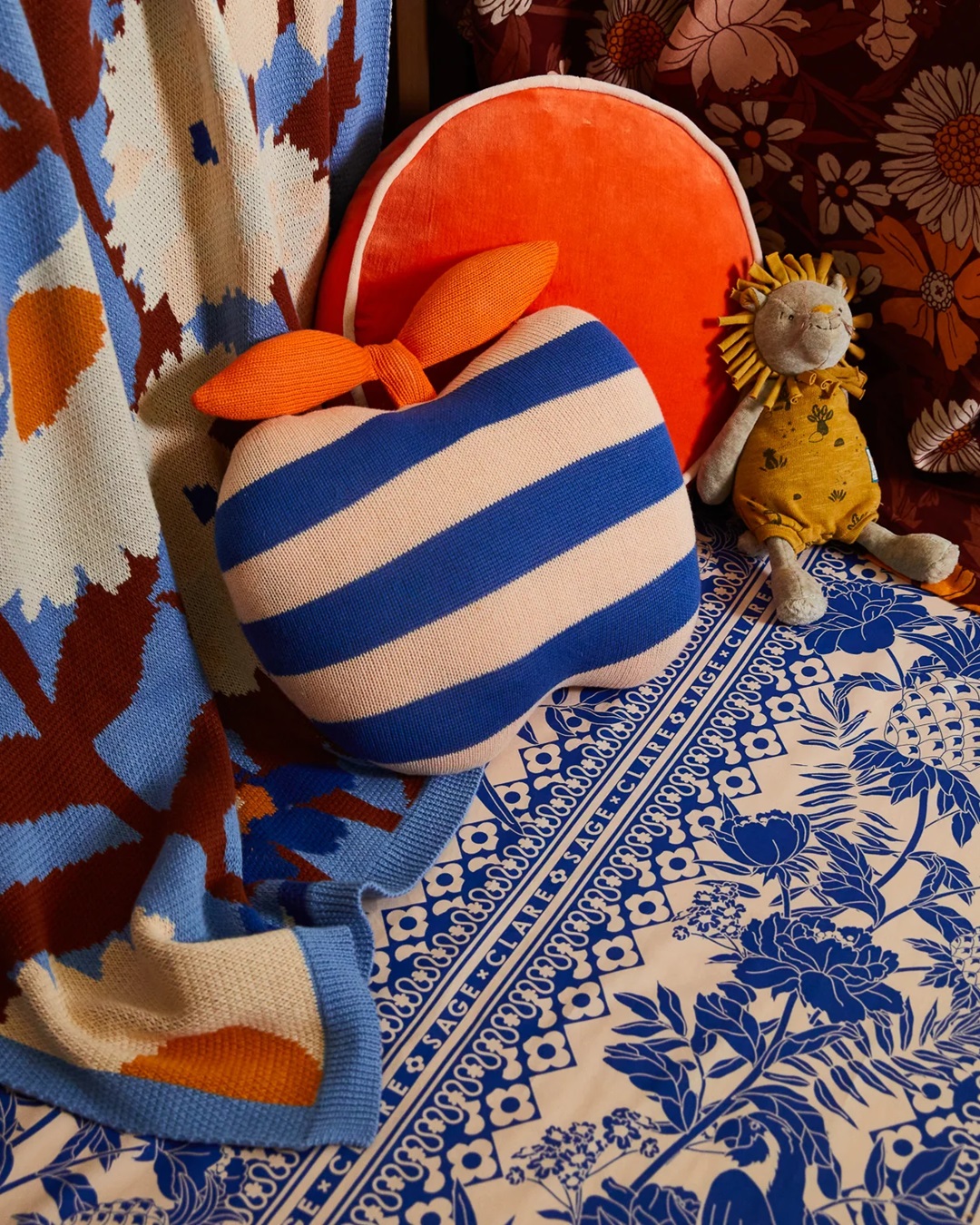 White and blue stripe apple cushion with orange leaves on floor with blue carpet and other cushions