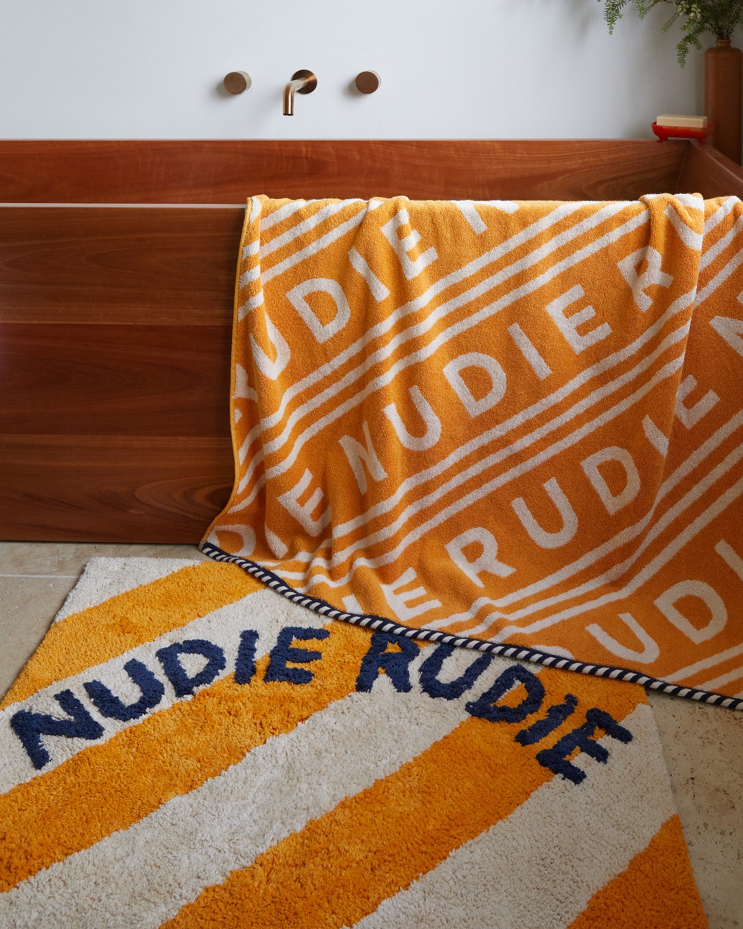 Gold and white stripe bath mat with Nudie Rudie on tiled floor